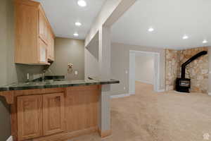 Bar featuring light brown cabinetry, a wood stove, sink, and light colored carpet