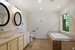 Bathroom featuring backsplash, tile patterned floors, vanity, tiled bath, and toilet