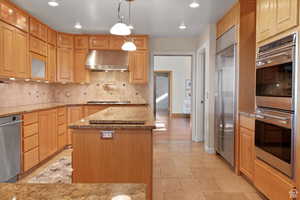 Kitchen with hanging light fixtures, light stone counters, extractor fan, a kitchen island, and appliances with stainless steel finishes