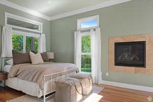 Bedroom with multiple windows, a fireplace, ornamental molding, and hardwood / wood-style flooring