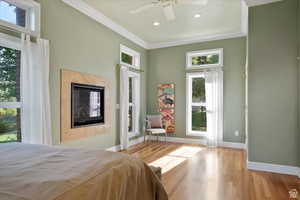 Bedroom with a tile fireplace, light hardwood / wood-style flooring, multiple windows, and ceiling fan