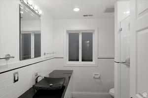 Bathroom featuring toilet, tile walls, and sink