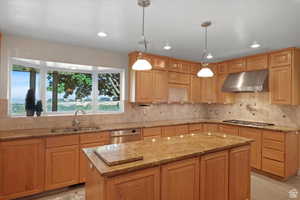 Kitchen featuring appliances with stainless steel finishes, extractor fan, sink, pendant lighting, and a center island