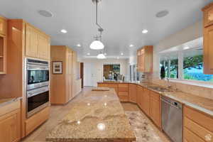 Kitchen featuring light stone countertops, stainless steel appliances, sink, light brown cabinets, and decorative light fixtures