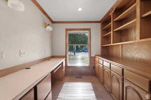 Interior space with wood walls, built in desk, light tile patterned floors, and crown molding