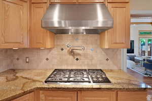 Kitchen with backsplash, light stone countertops, wall chimney exhaust hood, and stainless steel gas cooktop