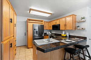 Kitchen featuring black appliances, sink, light tile patterned floors, kitchen peninsula, and a breakfast bar area