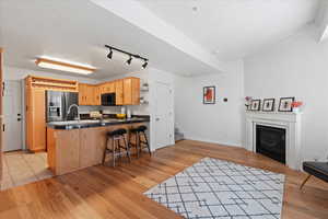 Kitchen with light brown cabinets, stainless steel fridge, ornamental molding, light hardwood / wood-style floors, and kitchen peninsula