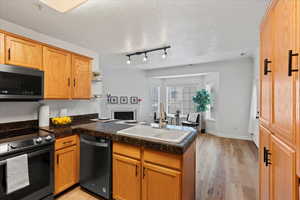 Kitchen featuring kitchen peninsula, appliances with stainless steel finishes, a textured ceiling, sink, and light hardwood / wood-style flooring