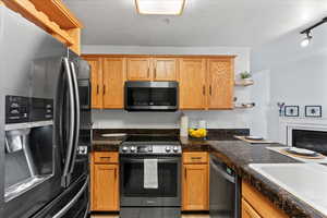 Kitchen featuring sink, dark stone countertops, a textured ceiling, track lighting, and appliances with stainless steel finishes