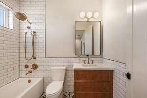 Full bathroom featuring tiled shower / bath combo, toilet, tile walls, and vanity