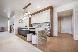 Kitchen featuring white cabinetry, hanging light fixtures, tasteful backsplash, light hardwood / wood-style floors, and a breakfast bar area