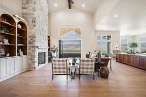 Dining space featuring beam ceiling, a fireplace, light hardwood / wood-style flooring, and high vaulted ceiling