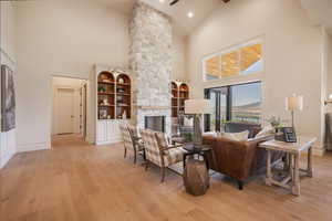 Living room featuring built in shelves, light hardwood / wood-style floors, high vaulted ceiling, and a stone fireplace