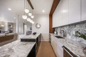 Kitchen with white cabinets, light hardwood / wood-style floors, hanging light fixtures, and sink