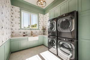 Clothes washing area with cabinets, ornamental molding, sink, an inviting chandelier, and stacked washer and clothes dryer