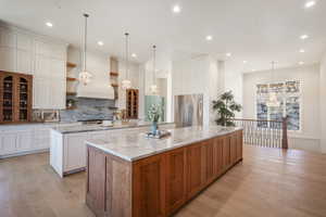 Kitchen featuring pendant lighting, built in refrigerator, custom range hood, a large island, and white cabinetry