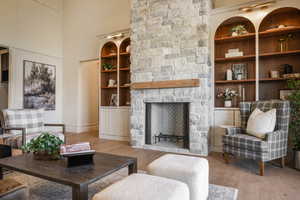 Living room featuring a fireplace, built in shelves, a towering ceiling, and light hardwood / wood-style flooring