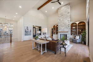 Living room featuring light wood-type flooring, ceiling fan, beam ceiling, high vaulted ceiling, and a stone fireplace