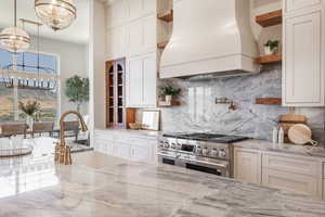 Kitchen featuring custom exhaust hood, a healthy amount of sunlight, double oven range, and light stone counters