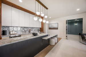 Kitchen with decorative backsplash, light wood-type flooring, light stone counters, white cabinets, and hanging light fixtures