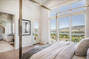 Bedroom with access to exterior, a water and mountain view, high vaulted ceiling, and light hardwood / wood-style flooring