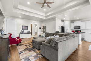 Living room featuring ceiling fan, a tray ceiling, and light hardwood / wood-style flooring