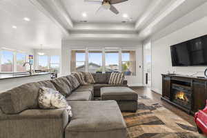 Living room featuring hardwood / wood-style flooring, a raised ceiling, ceiling fan, and a healthy amount of sunlight