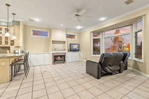 Living room featuring a gas fireplace, ceiling fan, crown molding, and light tile patterned floors