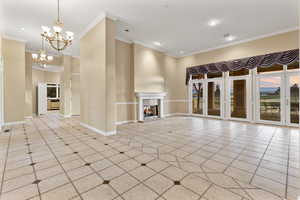 front entry/formal living room with a fireplace, light tile patterned floors, a chandelier, and ornamental molding