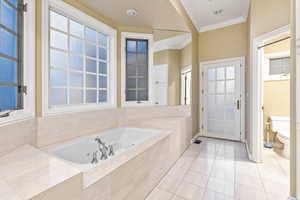 Primary bathroom featuring tile patterned floors, a relaxing garden tub, toilet, and ornamental molding. Door leading to private patio wired for hot tub