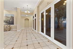 Corridor with an inviting chandelier, light tile patterned flooring, crown molding, and french doors