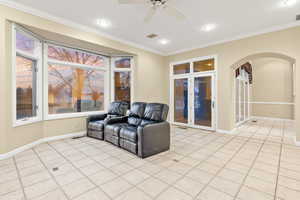 Tiled living room featuring ceiling fan and crown molding. Door leading to back covered patio.