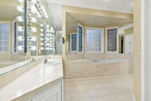 Primary Bathroom with tile patterned flooring, vanity, a relaxing tiled tub, and crown molding