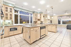 Kitchen featuring sink, decorative light fixtures, a center island with sink, dishwasher, and stainless steel microwave