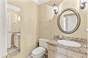 Bathroom off of kitchen featuring tile patterned flooring, vanity, toilet, and ornamental molding