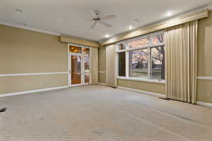 Carpeted primary bedroom with ceiling fan and ornamental molding. Door leading to covered back patio