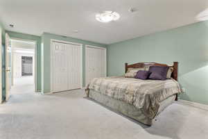 Basement bedroom with multiple closets, light carpet, and a textured ceiling