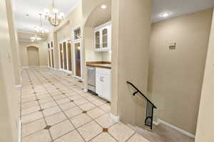 Showing hall at entry with crown molding, decorative light fixtures, a notable chandelier, and white cabinetry. Stairs leading to basement.