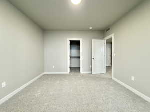 Unfurnished bedroom featuring a walk in closet, light carpet, and a closet