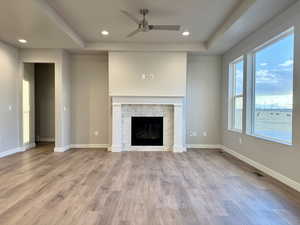 Unfurnished living room featuring a stone fireplace, ceiling fan, and light hardwood / wood-style floors