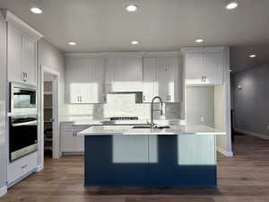 Kitchen with stainless steel oven, sink, hardwood / wood-style flooring, white cabinets, and an island with sink