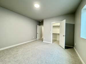 Unfurnished bedroom with light colored carpet, a walk in closet, and a closet