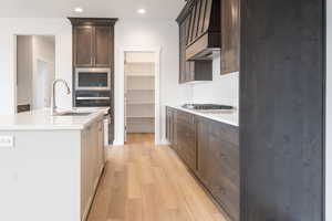 Kitchen with light wood-type flooring, tasteful backsplash, stainless steel appliances, sink, and a center island with sink