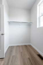 Walk in closet with light hardwood / wood-style flooring