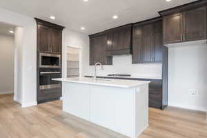 Kitchen with appliances with stainless steel finishes, light wood-type flooring, and a kitchen island with sink