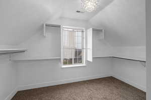 Spacious closet with carpet flooring, an inviting chandelier, and vaulted ceiling