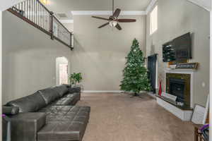 Carpeted living room featuring ceiling fan, a premium fireplace, a towering ceiling, and ornamental molding