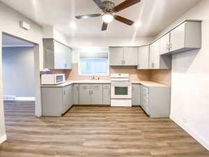 Kitchen with fresh paint, light gray cabinets, sink, white microwave, white appliances, and a new ceiling fan