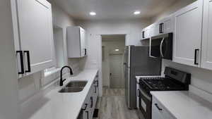 Kitchen featuring light stone countertops, white cabinetry, sink, appliances with stainless steel finishes, and light wood-type flooring